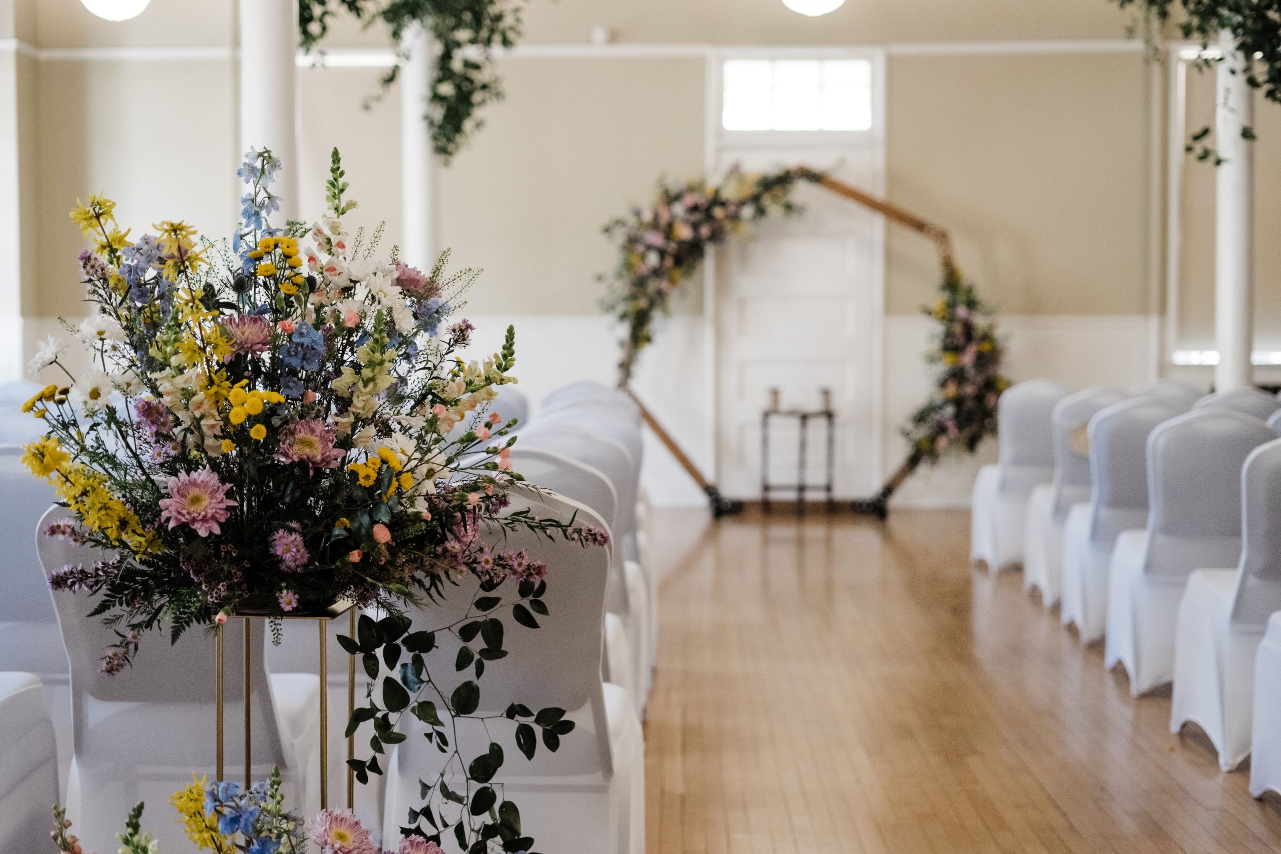 Amanda and Quintin Wedding Event layout - white fabric covered chairs and hexagon backdrop as the alter, with pastel floral spray in foreground