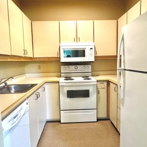 Kitchen with dishwasher, stainless sink, oven, microwave in hood, and refrigerator; All appliances are white. Cabinets are cream.